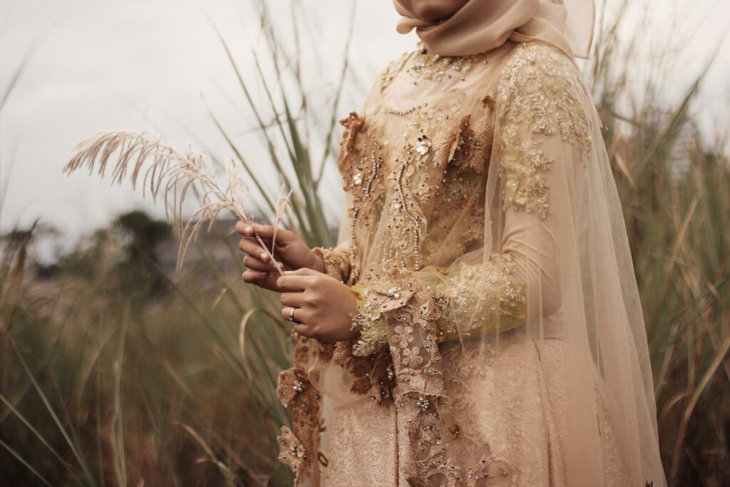 The Story Behind the NOOR Collection woman in beige floral embroidered wedding dress stands in grass field
